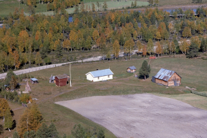 Eine Luftaufnahme eines Ranch mit verstreuten Gebäuden, umgeben von Bäumen, Häusern, Pfählen, einer Straße, Gras und Wasser.
