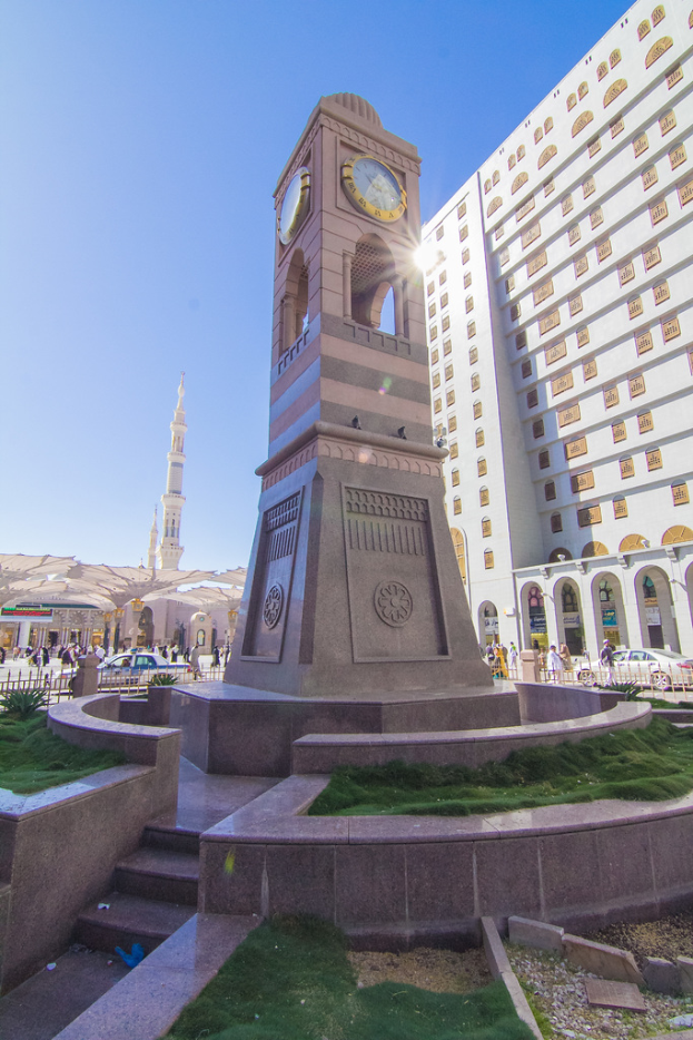 Ein Uhrenturm in der Mitte mit einem großen Gebäude rechts daneben.