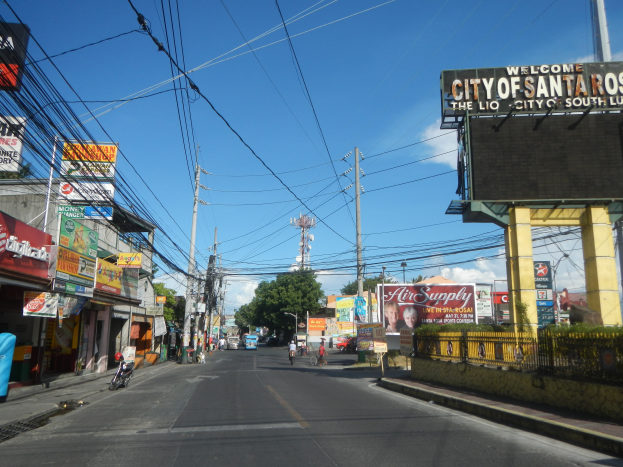 Eine belebte Stadtstraße mit Fahrzeugen, Radfahrern, Gebäuden und einem "Willkommen in Santa Rosa"-Schild auf der rechten Seite.