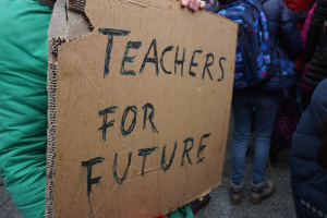Eine Person hält ein "Lehrer für die Zukunft"-Schild, steht zwischen einer Gruppe von Menschen mit Rucksäcken und Stiefeln.