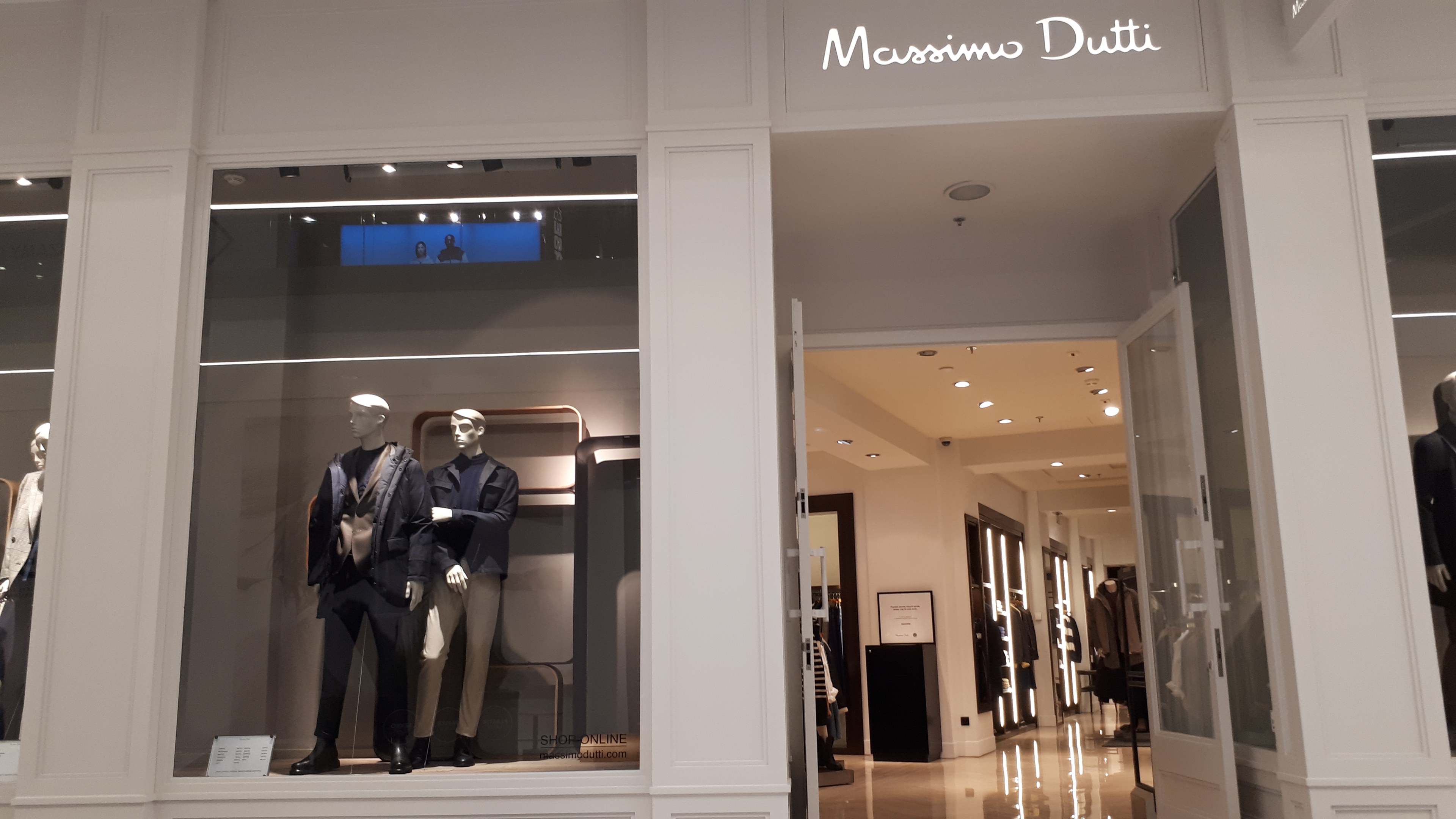 Innenansicht des Massimo Dutti Geschäfts in Mailand, Italien, mit Schaufensterpuppen in moderner Kleidung, beleuchteter Decke, Informationsschildern und sichtbarem Boden.