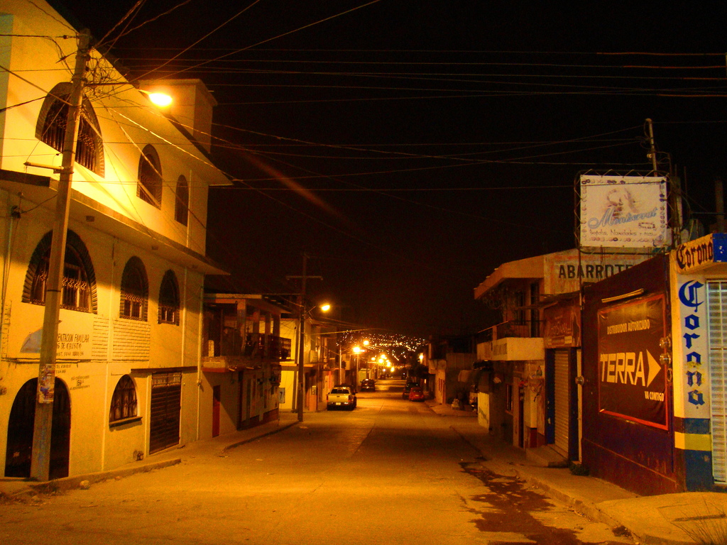 Eine Straßenszene mit Gebäuden und Strommästen auf beiden Seiten, einige geparkte Fahrzeuge vor den Gebäuden und eine Straße in der Mitte.