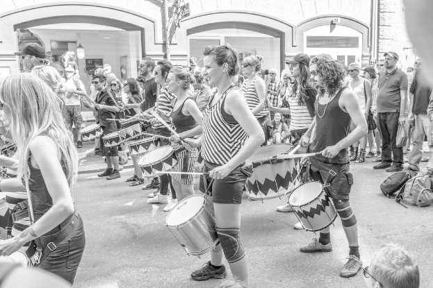 Eine Gruppe von Menschen, die draußen Musikinstrumente spielen, mit einer geschlossenen Glastür und einem Licht im Hintergrund.