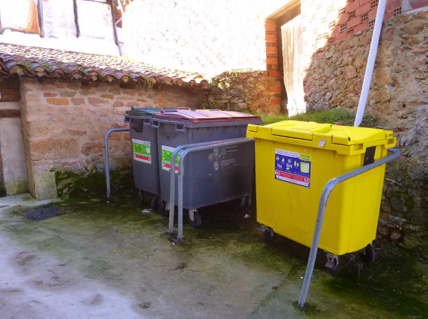 Zwei gelbe und graue Mülltonnen stehen nebeneinander vor einem Gebäude mit einer Wand und einem Fenster im Hintergrund.