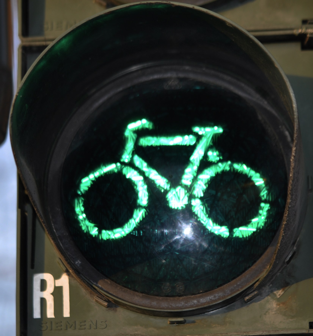 Grünes Ampelsignal mit Fahrradsymbol, das an einer Wand beleuchtet ist.