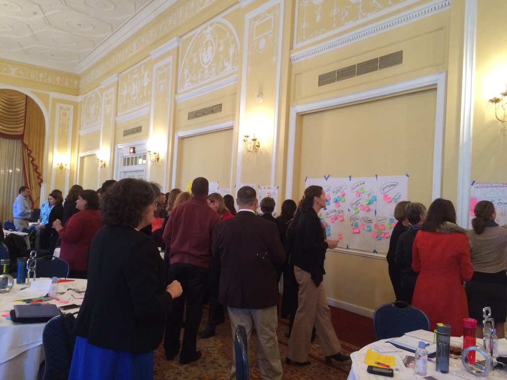 Eine Gruppe von Menschen untersucht Plakate und Diagramme, die an einer Wand in einem scheinbar Kunstmuseum angebracht sind.