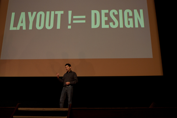 Eine Person steht auf einer Bühne und spricht, mit einem Bildschirm mit Text dahinter.