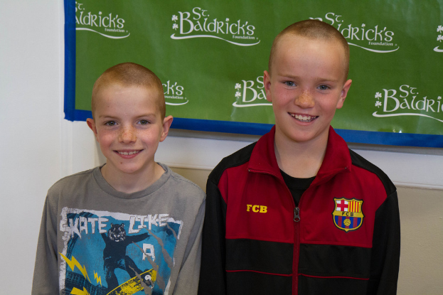 Zwei Jungen stehen zusammen, lächeln, mit einem Banner im Hintergrund mit Text.