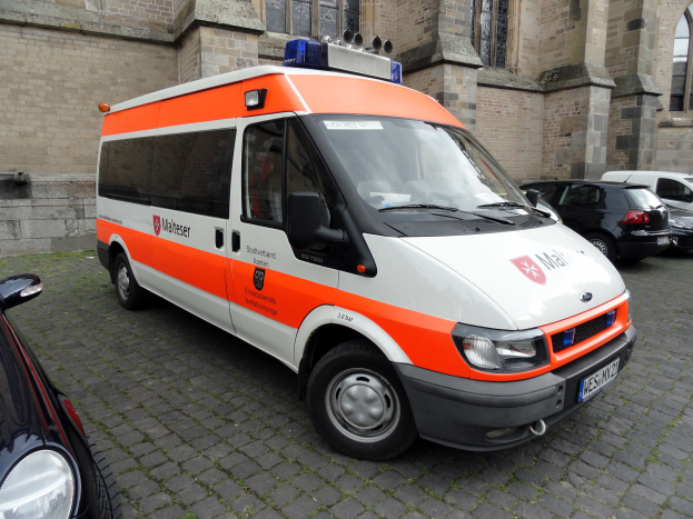 Ein Rettungswagen steht vor einem Gebäude mit Fenstern, umgeben von anderen Fahrzeugen auf der Straße.