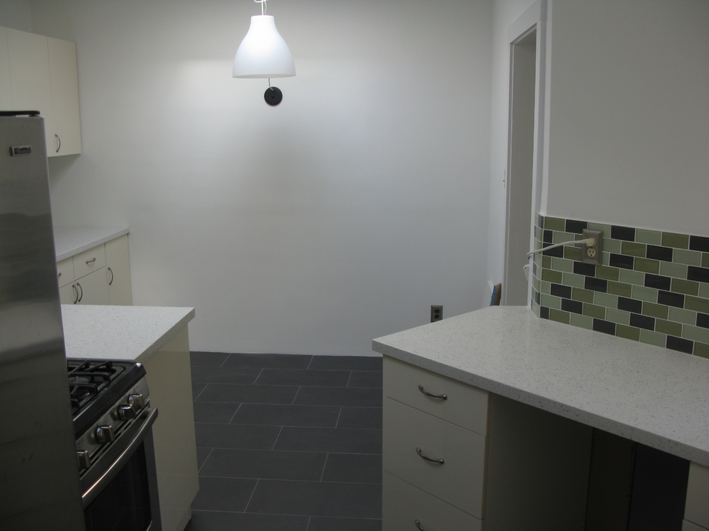 Eine Küchenzeile mit Schränken, einem Ofen, einem Gasherd, einem Kühlschrank und einer Leuchte.