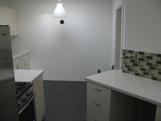 Eine Küchenzeile mit Schränken, einem Ofen, einem Gasherd, einem Kühlschrank und einer Leuchte.