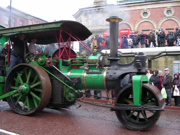 Ein Motor ist zentral in einem Bild positioniert, mit Gebäuden oben und Menschen auf der rechten Seite des Bildes.