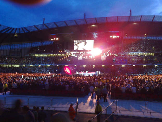 Eine Konzerthalle mit Menschen, Bühnenlichtern und einem Projektionsschirm.