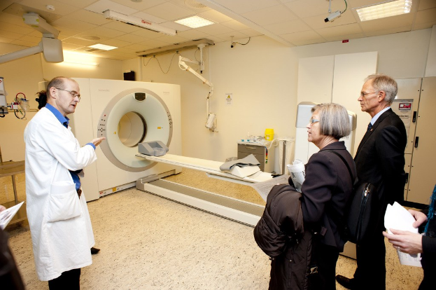 Arzt in weißer Uniform erklärt eine CT-Scan-Maschine zwei Personen in schwarzen Mänteln