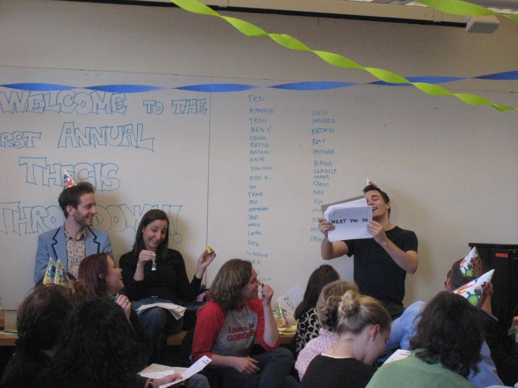 Eine Gruppe von Menschen feiert ihren ersten jährlichen Thesendurchwurf, mit Bändern auf dem Dach und einigen Individuen mit Mützen.