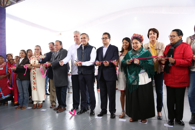Eine Gruppe von Menschen bei einer Scherenschnitte-Zeremonie, die lächeln und eine Schere halten, mit einer Säule links, verstreuten Papieren auf dem Boden und einem weißen Tuch im Hintergrund.