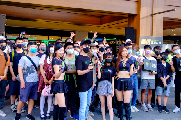 Eine Gruppe von Menschen steht vor einem Gebäude, einige tragen Masken und halten Gegenstände in den Händen, mit einem Transparent, Lautsprechern und Lampen im Hintergrund, was auf eine Demonstration in Hong Kong hinweist.