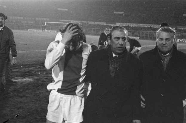 Eine Gruppe enttäuschter Männer in Schwarz-Weiß-Kleidung steht zusammen auf einem Fußballfeld, mit einem Stadion im Hintergrund, wahrscheinlich nach einem gewonnenen Spiel.