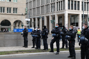 Polizisten in schwarzen Uniformen und Masken stehen vor einem Berliner Gebäude mit Glasfenstern, Säulen und umgebenen Infrastruktur.