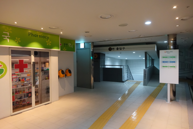 Der Eingang zu einer Apotheke mit einem "Apotheke"-Schild auf der linken Seite, einer Tafel mit Text auf der rechten Seite und beleuchteten Lichtern auf dem Dach.