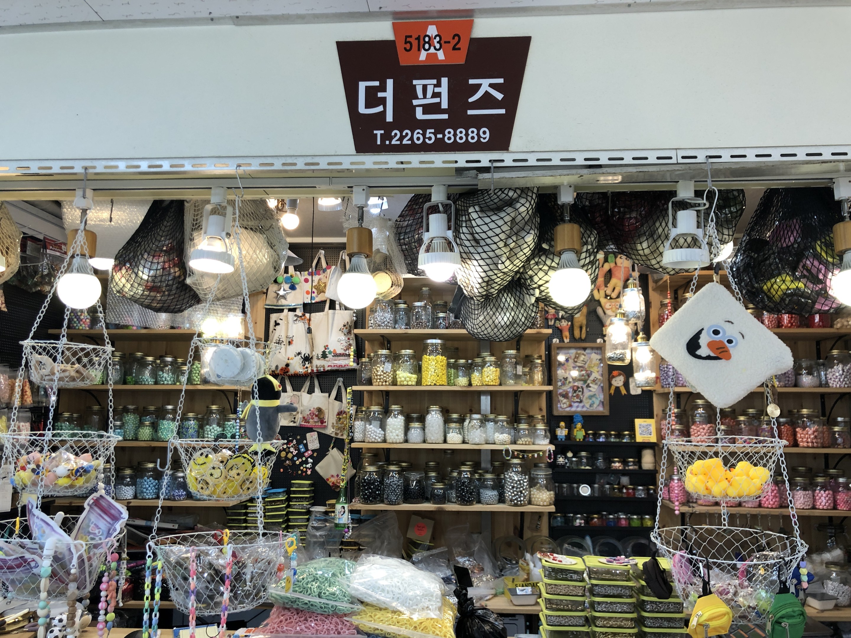 Ein unordentlicher Laden in Seoul, der verschiedene Gegenstände wie Körbe, Lichter, Flaschen und Spielzeuge auf Regalen ausstellt, mit einer Tafel öber dem Eingang, die ihn als bestbewerteten koreanischen Shop ausweist.