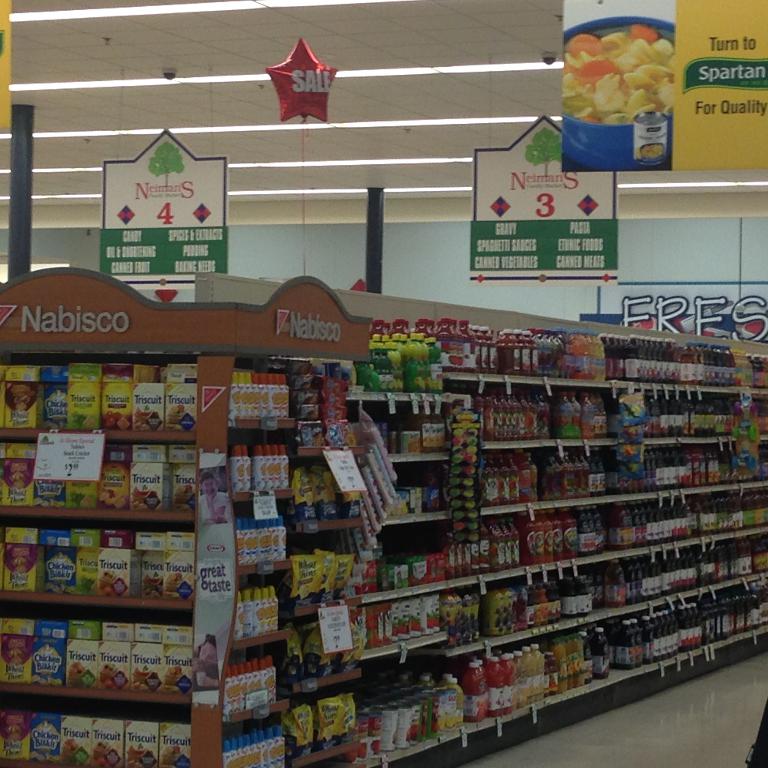 Ein Supermarktinneres mit Regalen voller Lebensmittel, Deckenleuchten und Schildern.